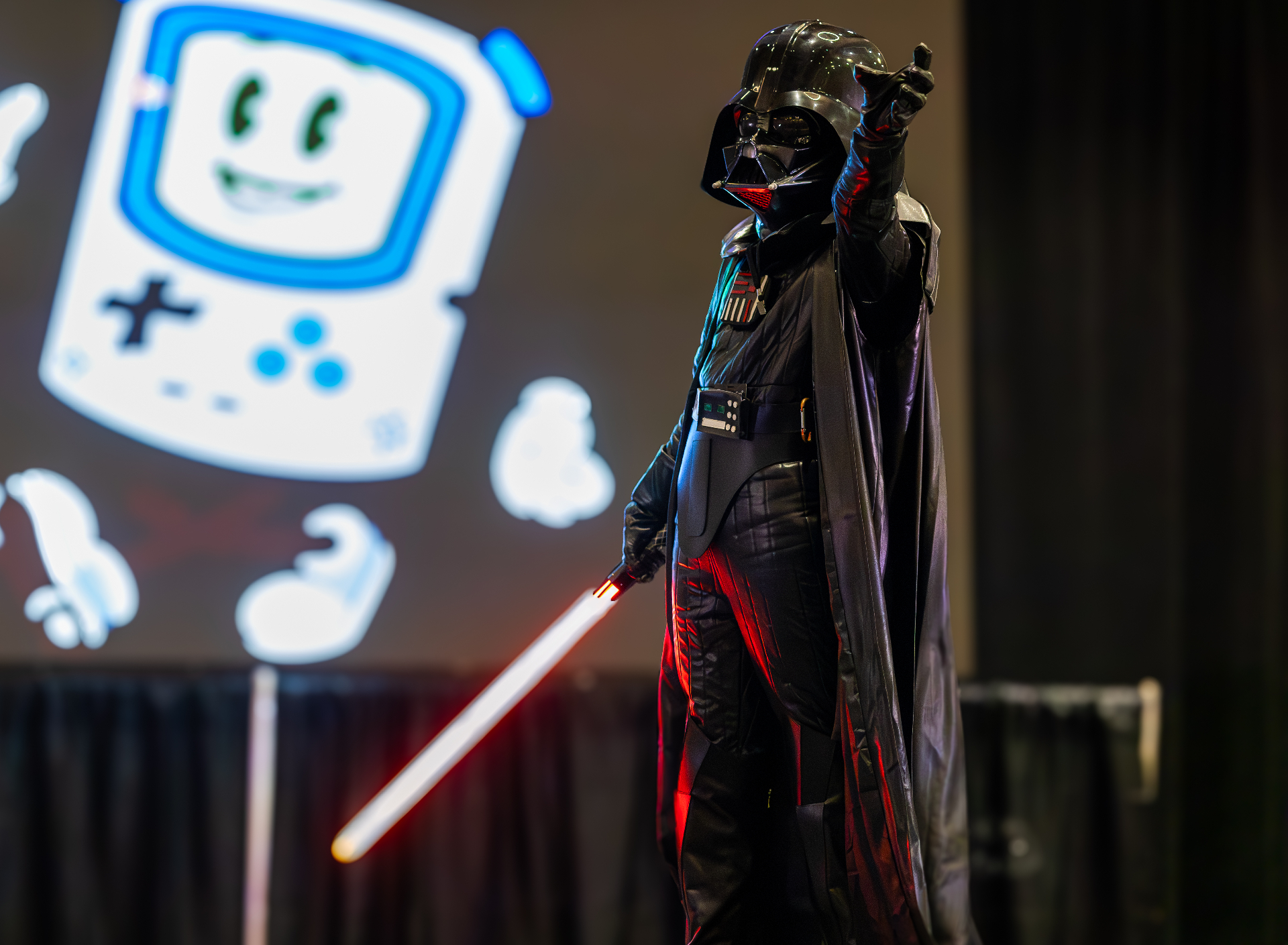 Darth Vader cosplayer on stage with lightsaber at a convention event