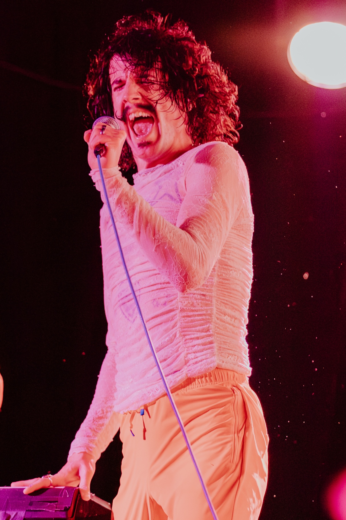Vocalist screaming into microphone in pink stage lighting